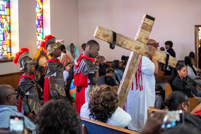 Mar 24, 2024; Columbus, OH; Revered Fred Booker dressed as Jesus carries a cross through the aisle as kids dressed as soldiers follow him during an Easter performance at the Family Missionary Baptist Church on Palm Sunday. The performance reenacted several scenes from the crucifixion, last dinner and resurrection of Jesus.